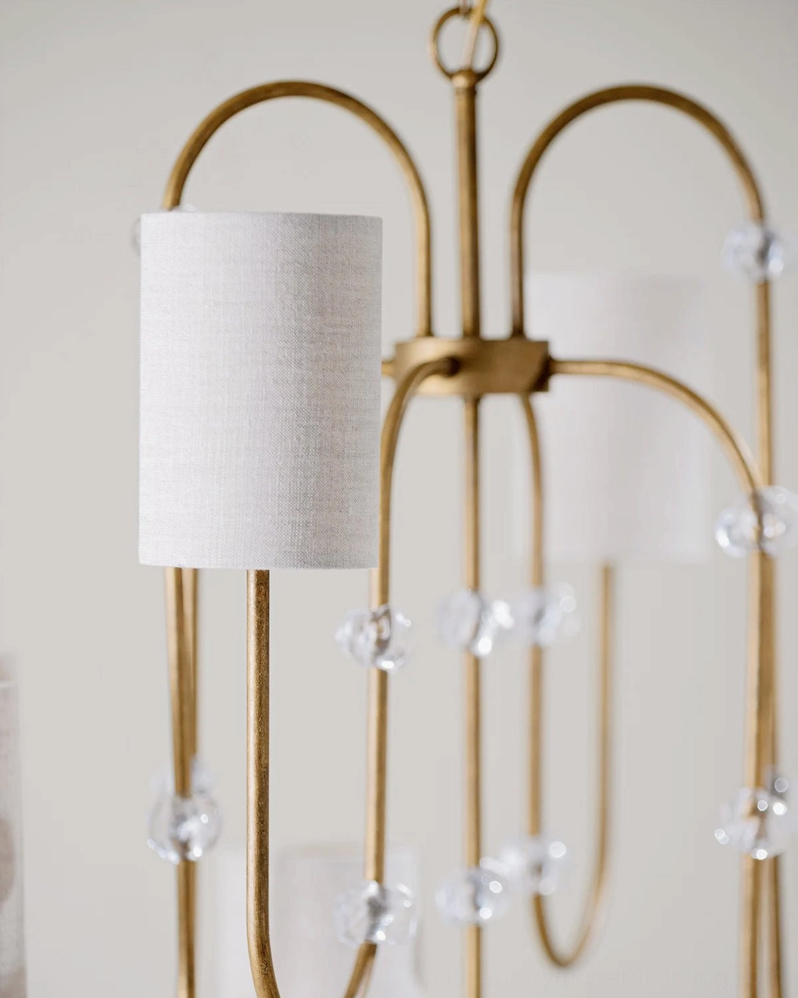 Close-up detail of Tanyel chandelier showing crystal beads, white fabric shade, and curved brass arm craftsmanship