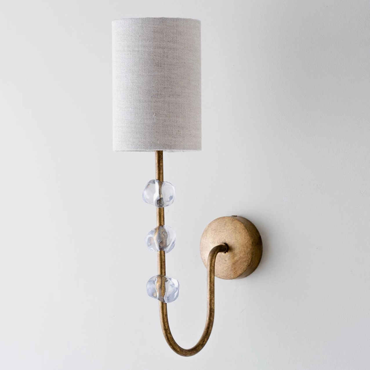 Tanyel single-arm wall sconce with curved brass rod and cylindrical shade on white background