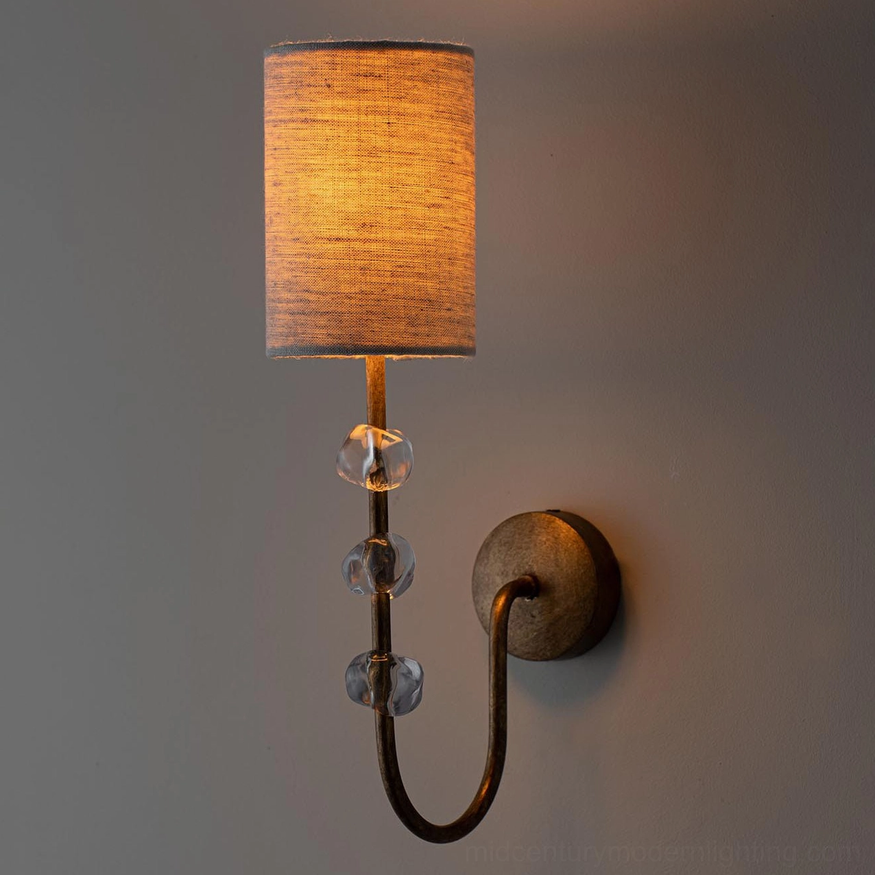 Tanyel single-light wall sconce with dark bronze frame and glowing amber lampshade against dark wall