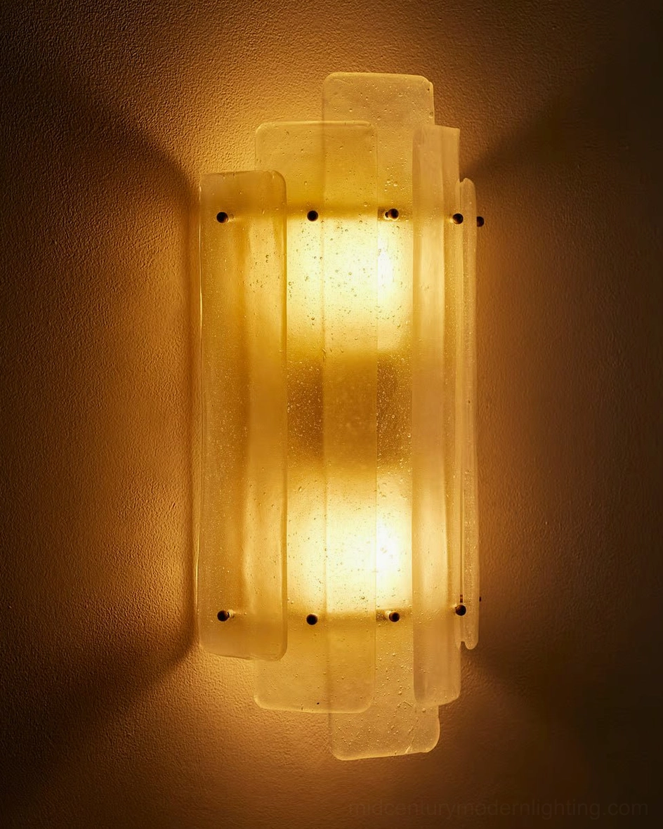 Close-up frontal view of Tasha sconce with amber-glowing seeded glass and brass fasteners