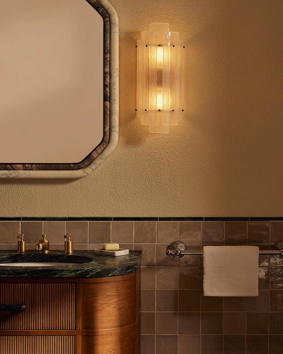 Tasha brass and glass sconce lit above wood cabinet in bathroom with warm ambient light