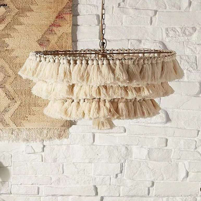 Cream tiered tassel pendant light with gold metal detailing against white brick wall with kilim rug accent