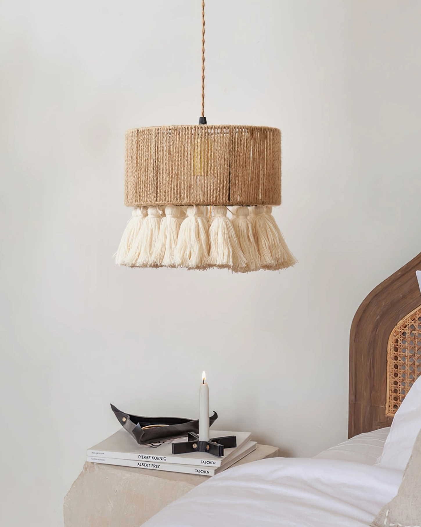 Tassel pendant lamp hanging above wooden bedside area, soft warm light diffusion through jute weave, boho aesthetics