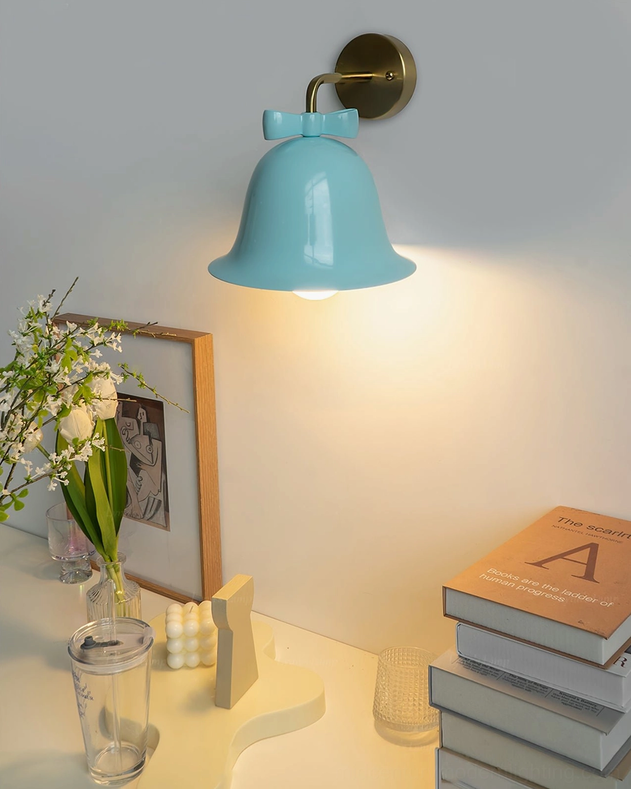 Teal blue Bow Bell Wall Lamp illuminating reading corner with stacked books and flowers, calm cozy home lighting