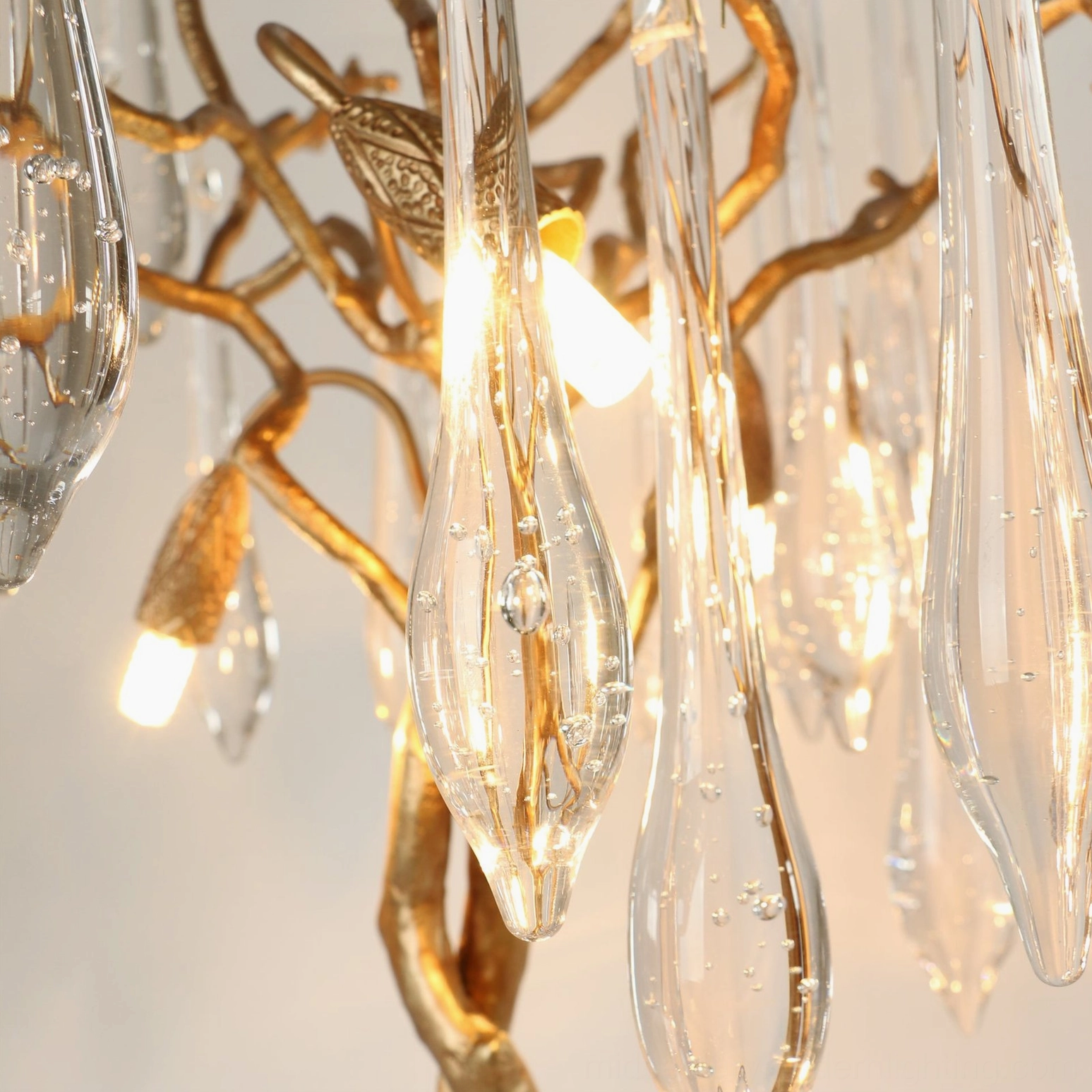 Close-up detail of crystal clear glass teardrop pendants hanging from gilded metal branches showing light refraction