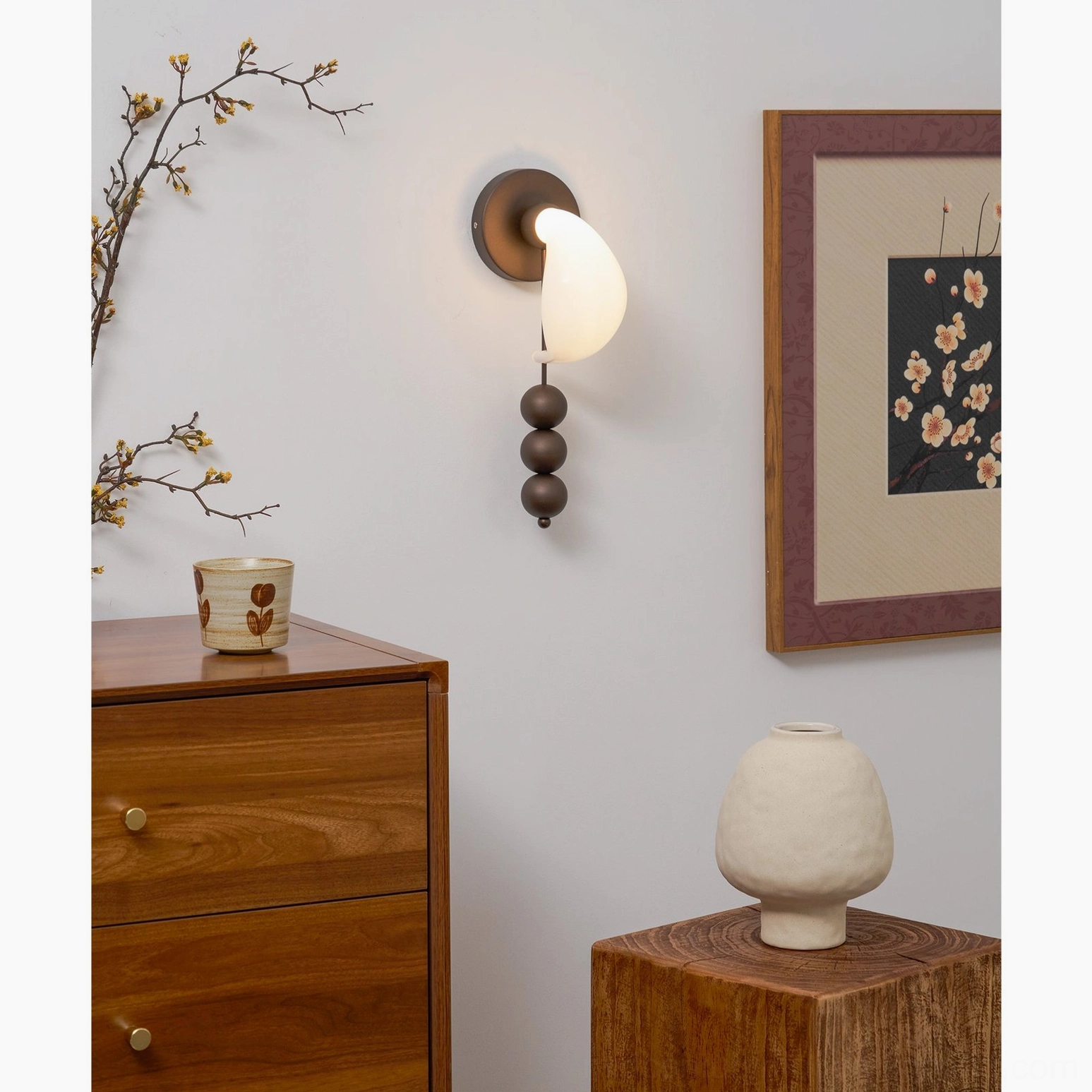 Teardrop glass wall sconce with sculptural metal base positioned in bedroom bedside setting, bronze finish with warm glowing illumination