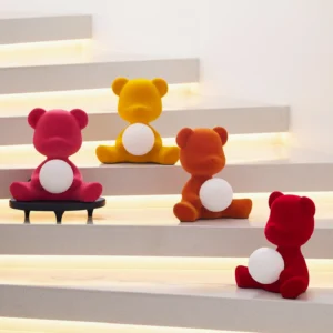 Collection of multi-colored teddy bear table lamps in various sizes and finishes illuminated on modern staircase