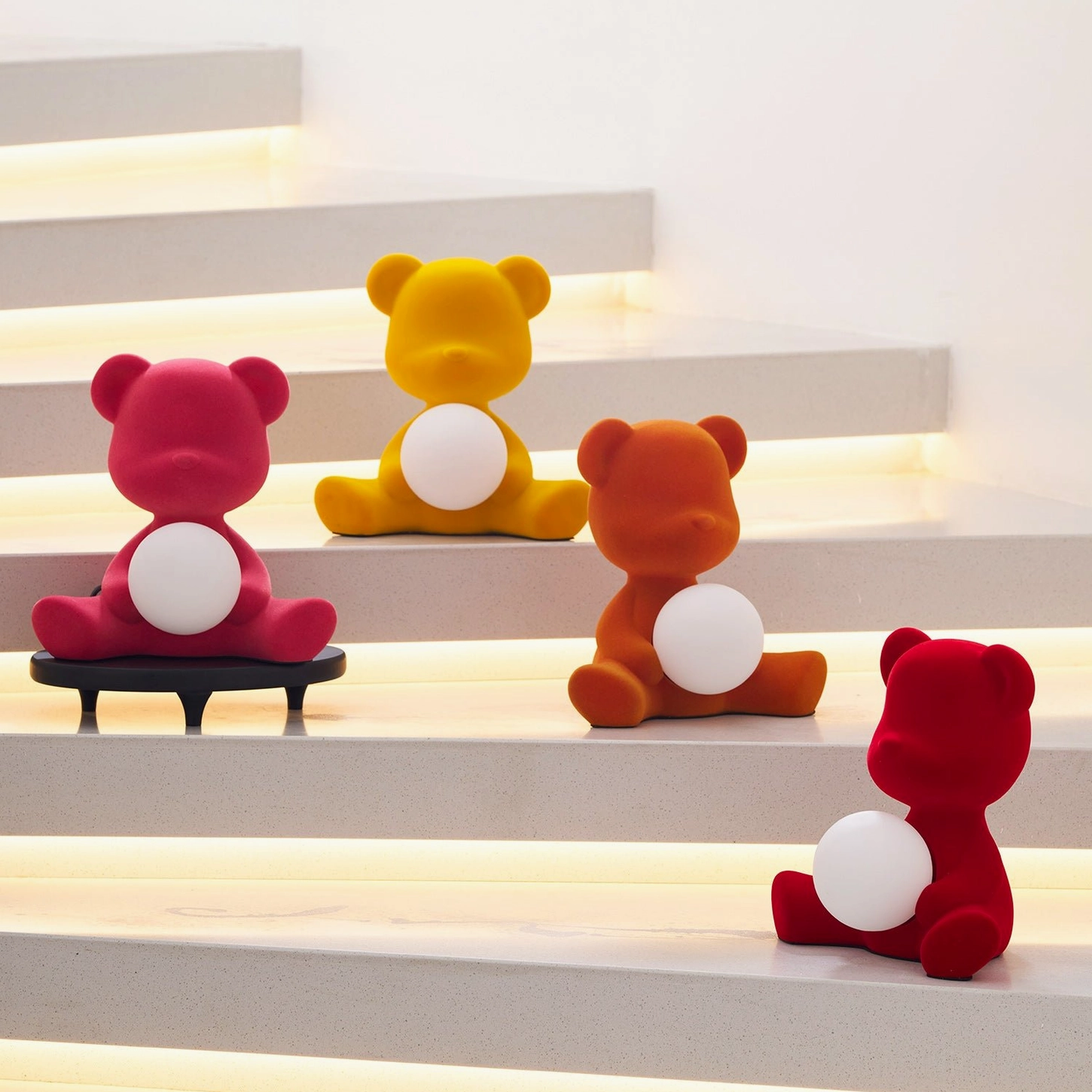 Collection of multi-colored teddy bear table lamps in various sizes and finishes illuminated on modern staircase