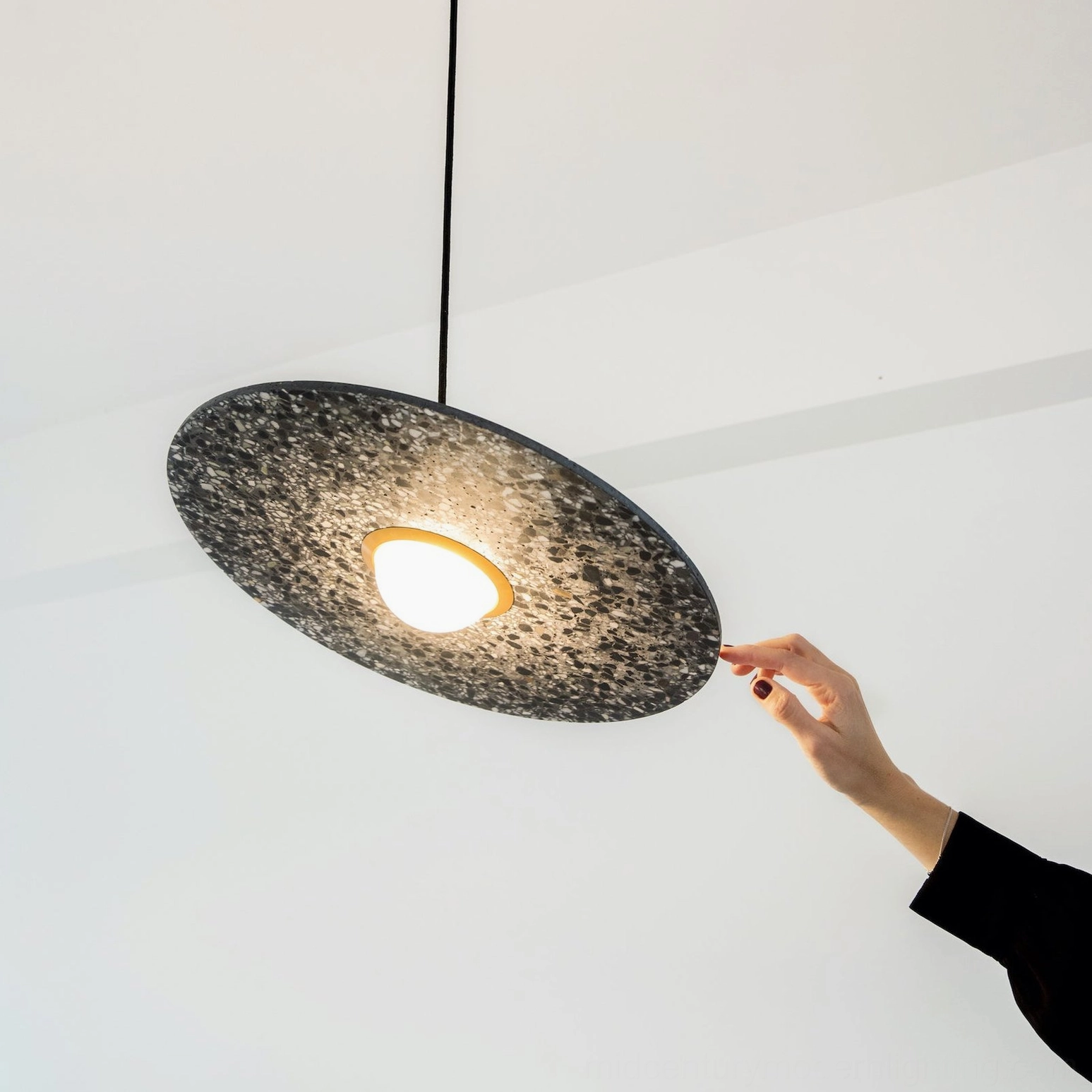 Hand adjusting dark terrazzo pendant lamp showing warm LED light glow and textured finish close-up
