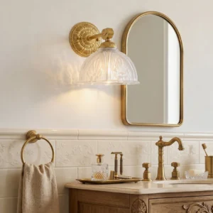 Thayer brass wall sconce installed on either side of arched gold-frame bathroom vanity mirror