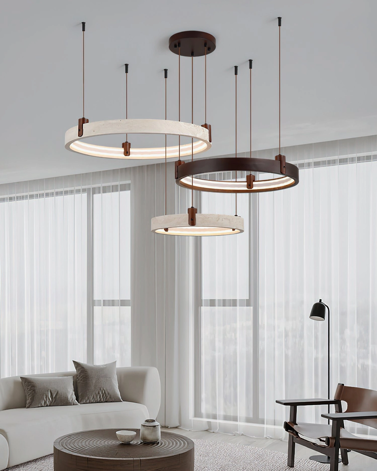 Three-tier travertine ring chandelier in sunlit minimalist living room, showcasing soft warm ambient lighting and two-tone wabi-sabi design