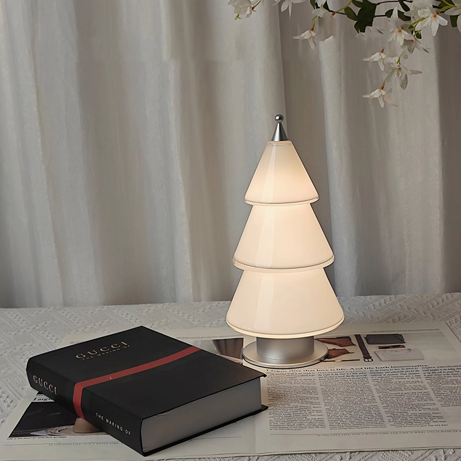 Faceted cone table lamp with warm glow on modern reading desk surrounded by books and newspapers Nordic style