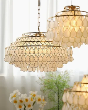 Multiple tiered shell pendant lamps in close-up, indoor setting with sheer curtains, floral and green plant decor, warm glowing vintage lighting
