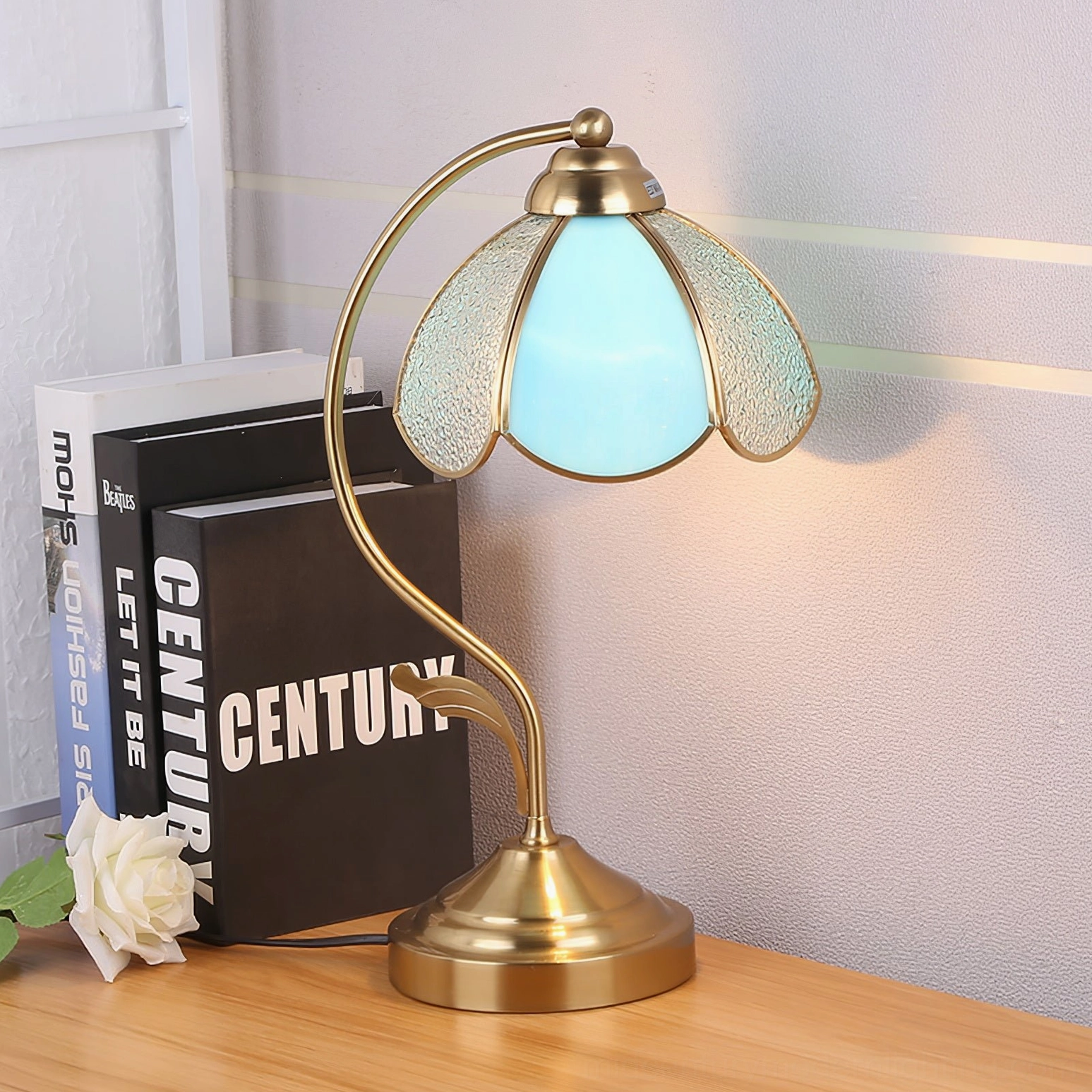 Side view of blue-tinted Tiffany table lamp with textured glass shade on wooden desk with botanical decor