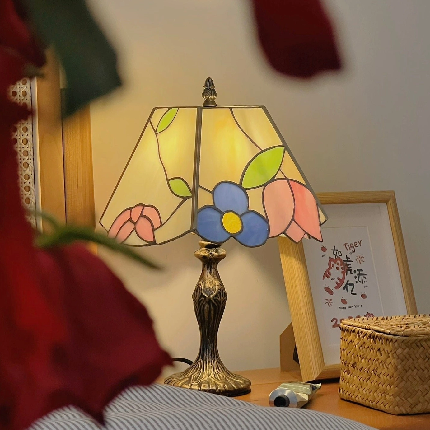 Vintage Tiffany lamp with floral stained glass shade on bedroom nightstand with rose foreground