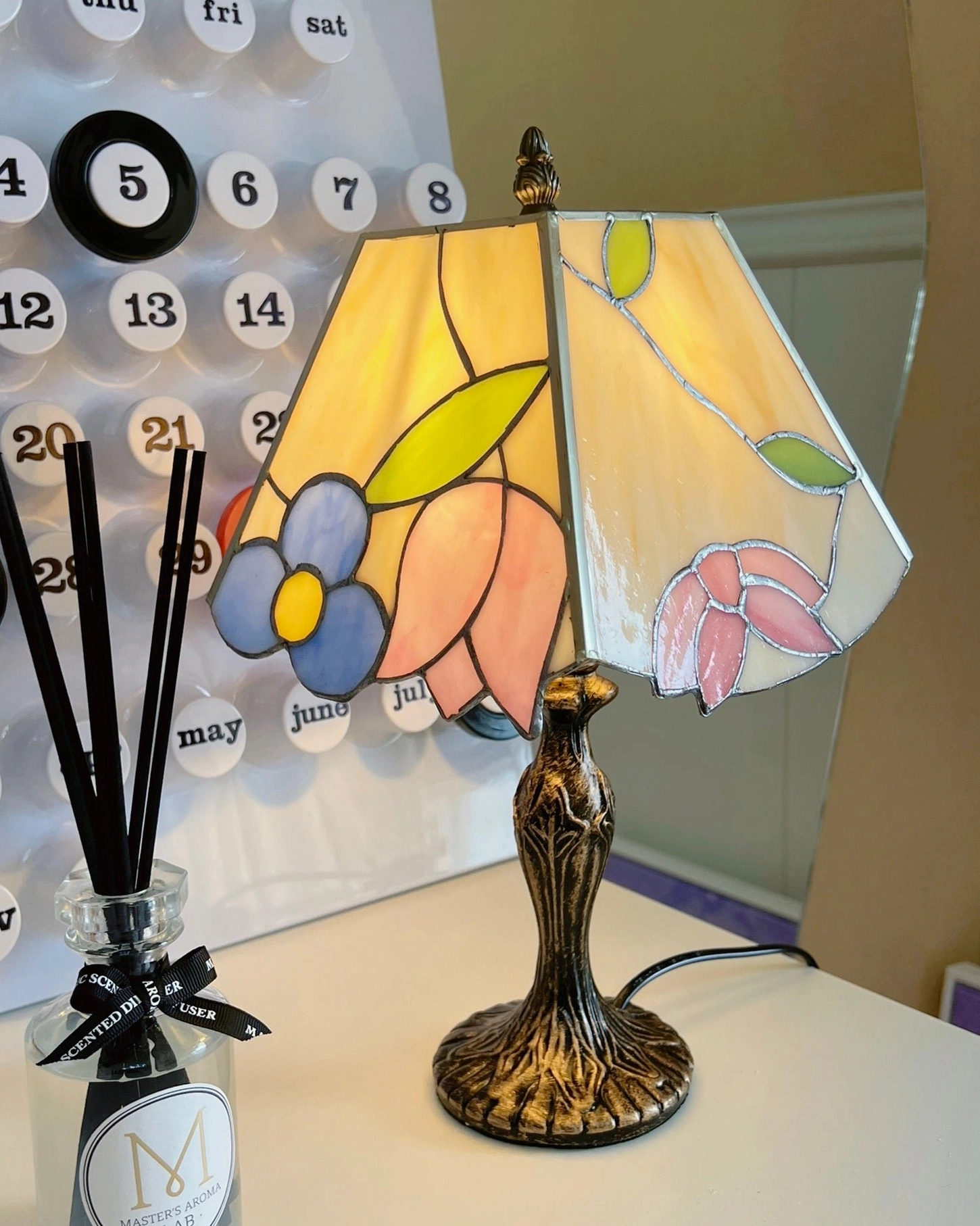Handcrafted Tiffany stained glass lamp on home desk with reed diffuser and calendar backdrop