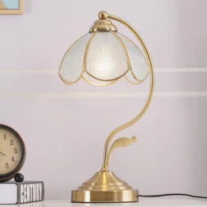 Frosted opaque Tiffany table lamp with elegant curved brass frame displayed on tabletop with decorative books and clock