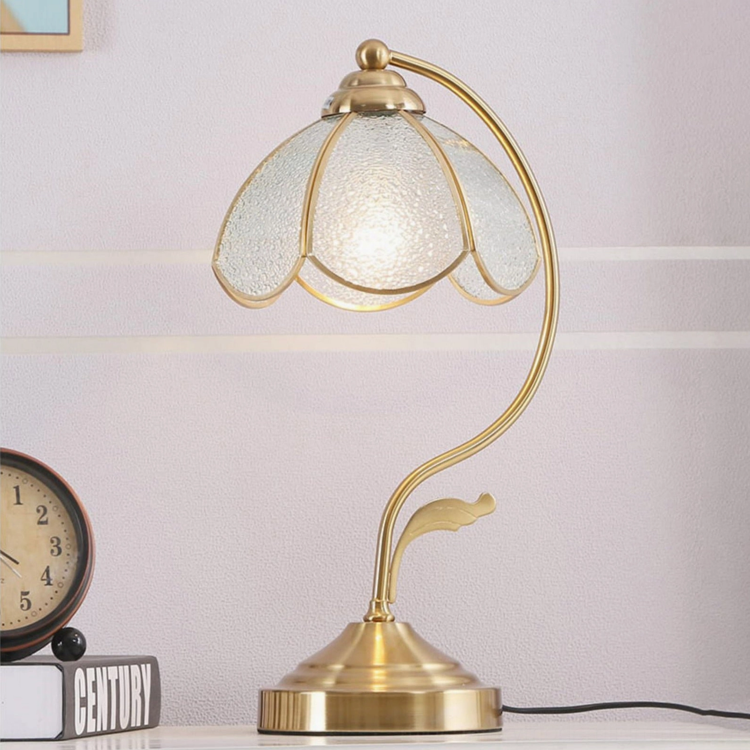 Frosted opaque Tiffany table lamp with elegant curved brass frame displayed on tabletop with decorative books and clock