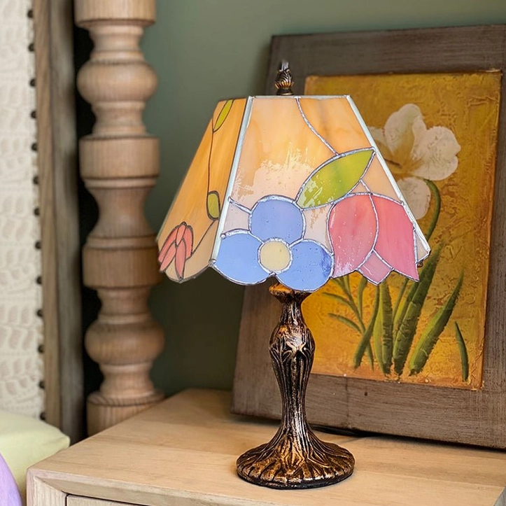 Art Nouveau style Tiffany glass lamp on wooden dresser with bronze pedestal base side view