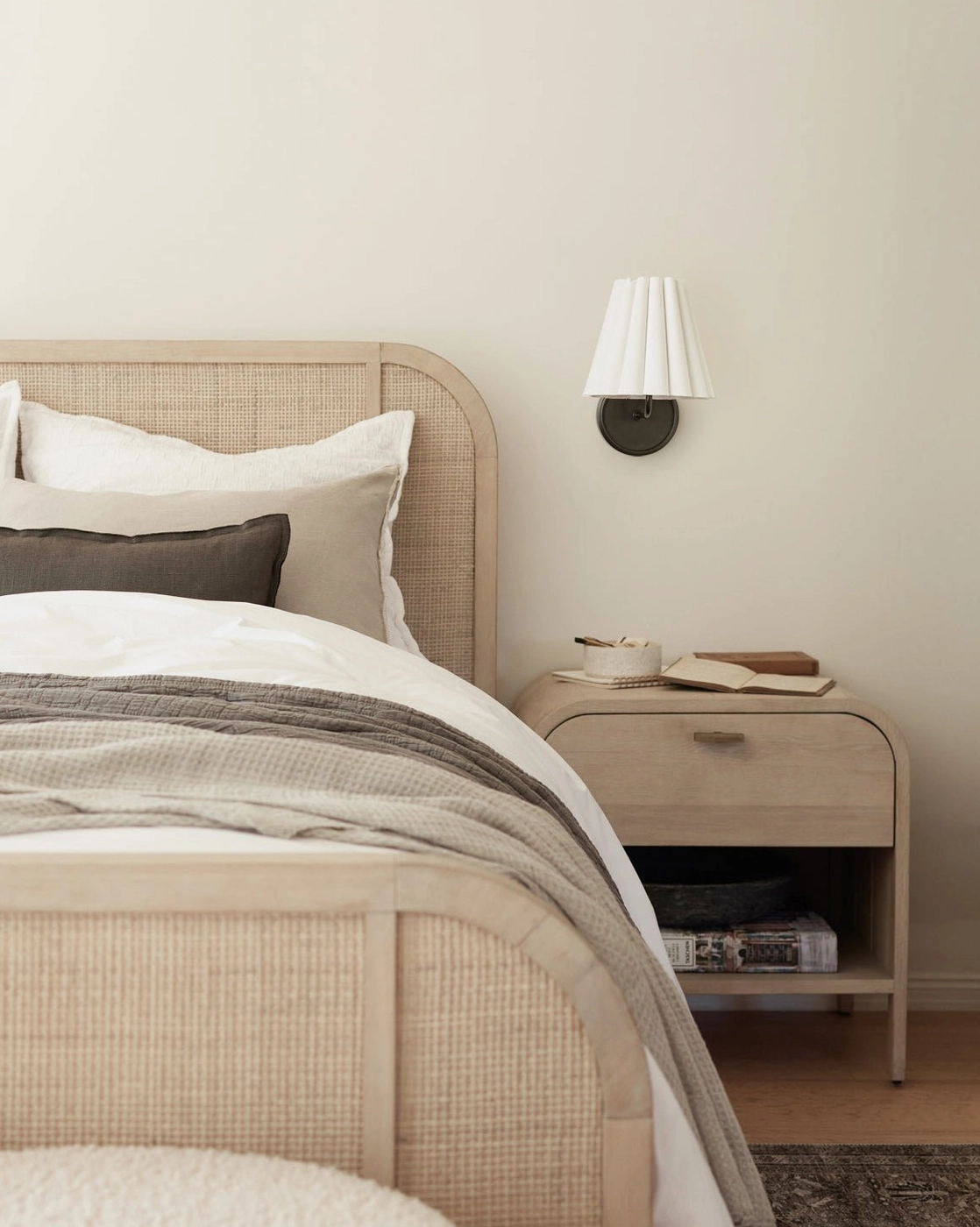 Dark metal Tilia wall sconce in cozy bedroom with rattan bed frame and neutral tones