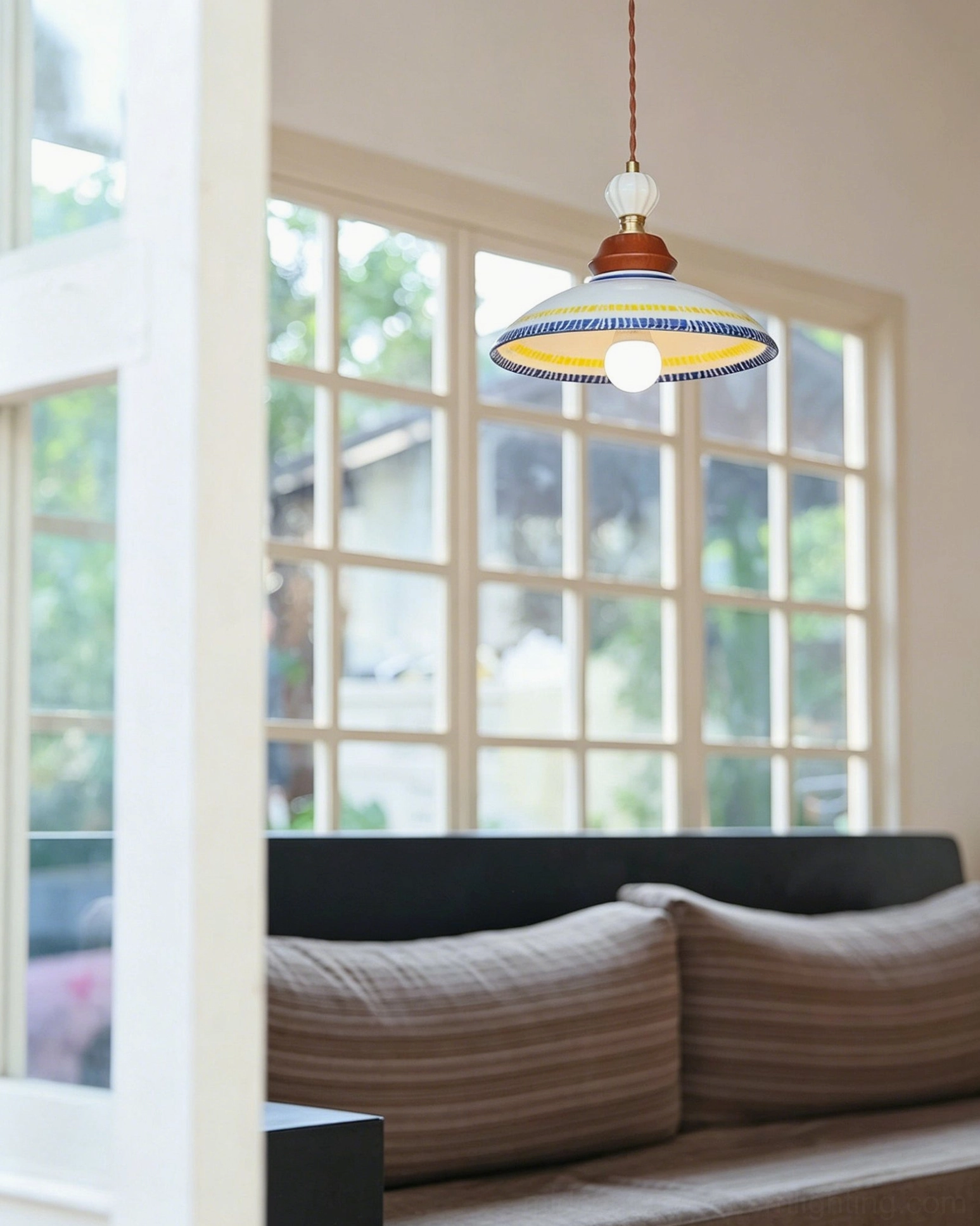 Tilly ceramic pendant with exposed white globe LED bulb hanging in living room setting with grid window and modern sofa beneath