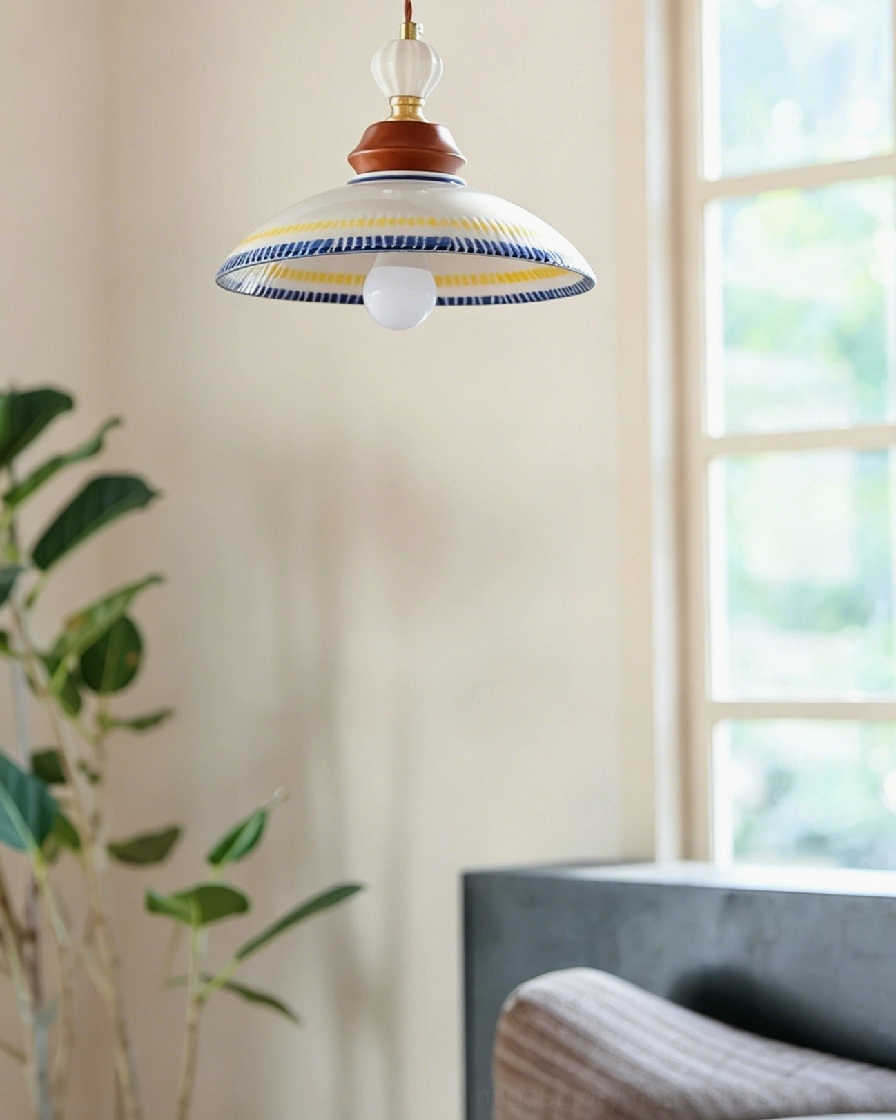 Tilly ceramic pendant light with white base and coordinated blue and yellow decorative lines suspended in beige interior space with green plant and window