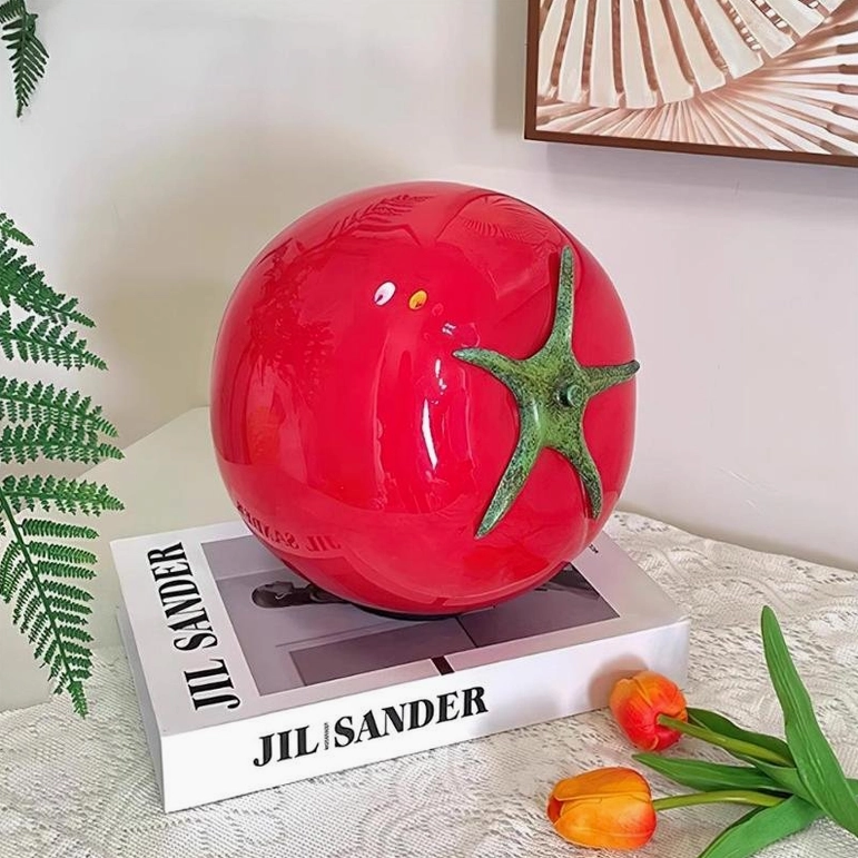 Red tomato glass lamp on bedroom dresser with fashion book and tulip decoration, three-quarter view