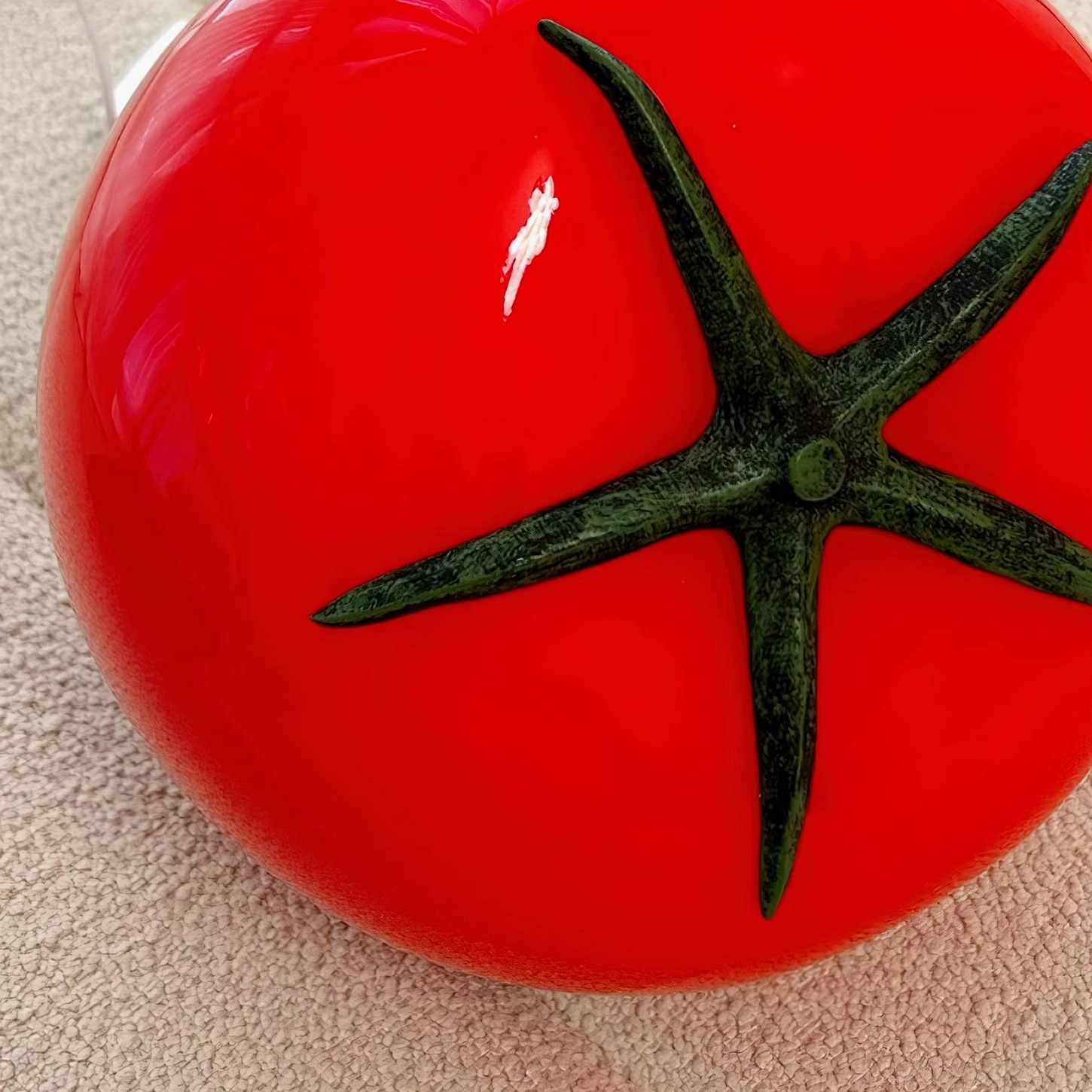 Close-up detail of red tomato glass lamp showing glossy finish and green calyx