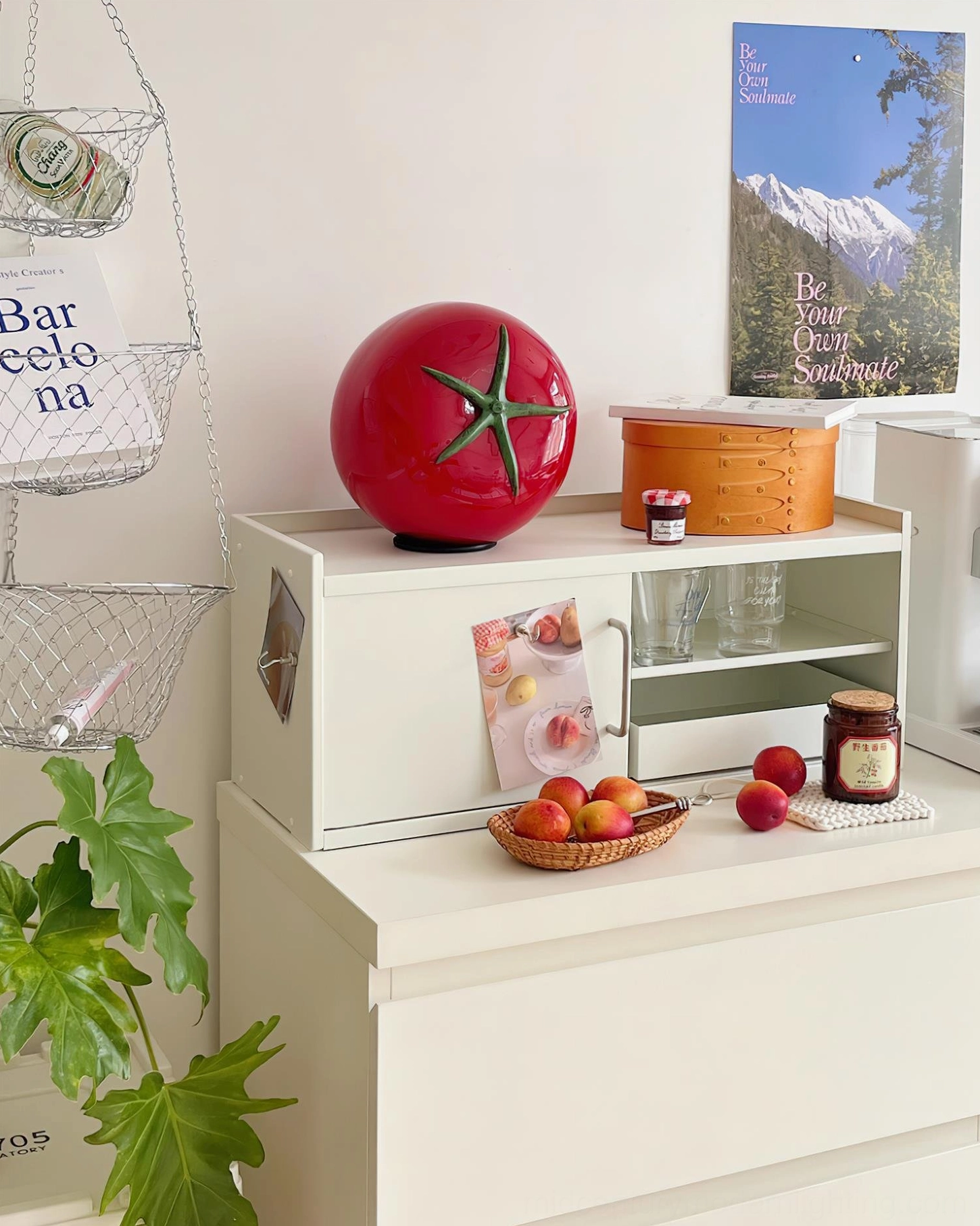 Tomato glass lamp on white dresser with travel poster and green potted plants