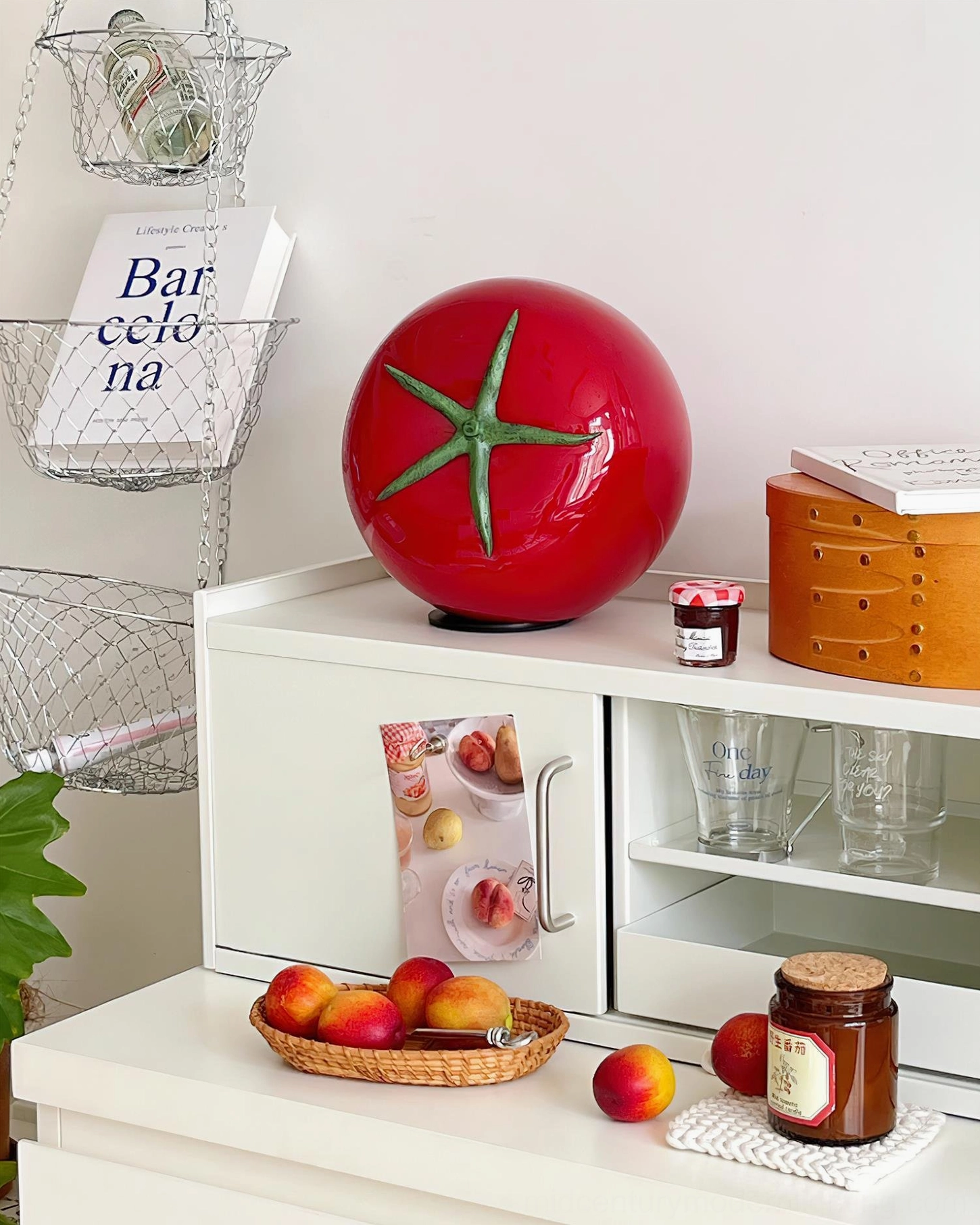 Red tomato glass table lamp on kitchen countertop with fresh fruits and storage jars