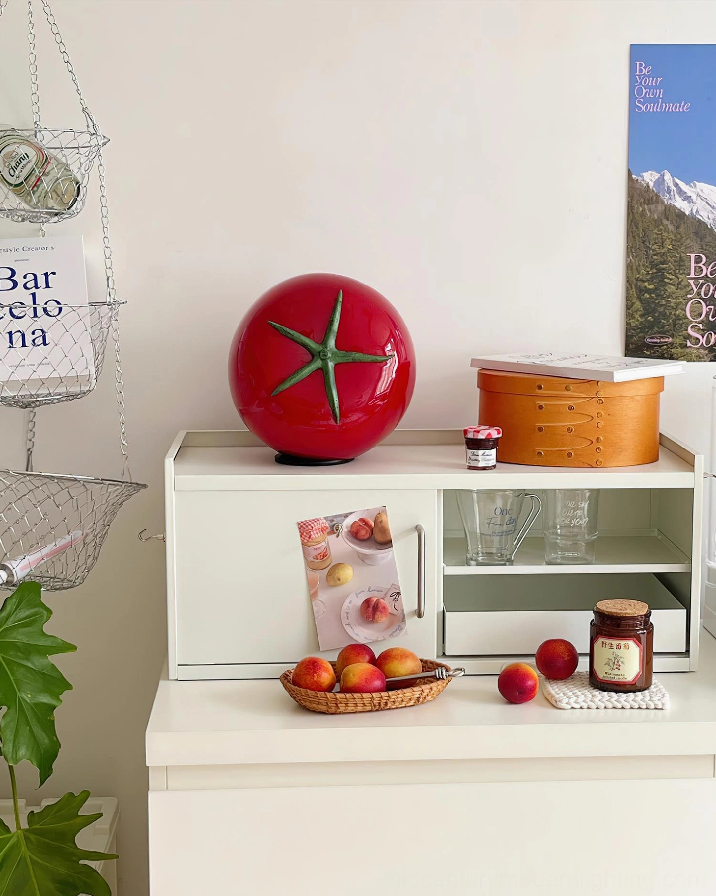 Red tomato glass lamp front three-quarter view on dresser with fruits and decorative jars