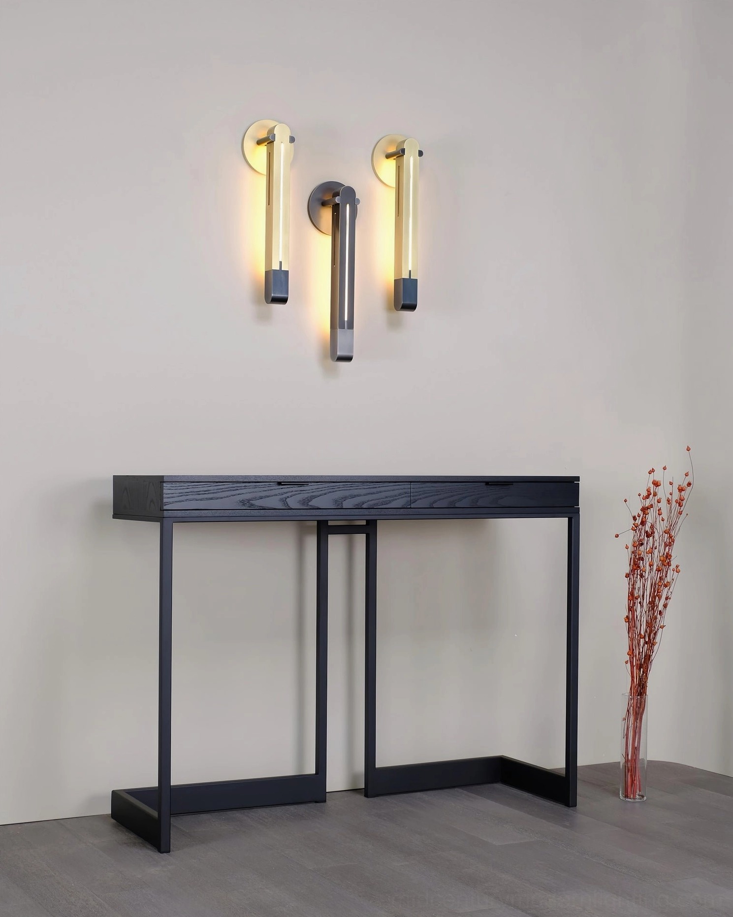 Set of three Torpedo wall sconces in black and brass finishes installed in hallway with black console table and dried floral decor