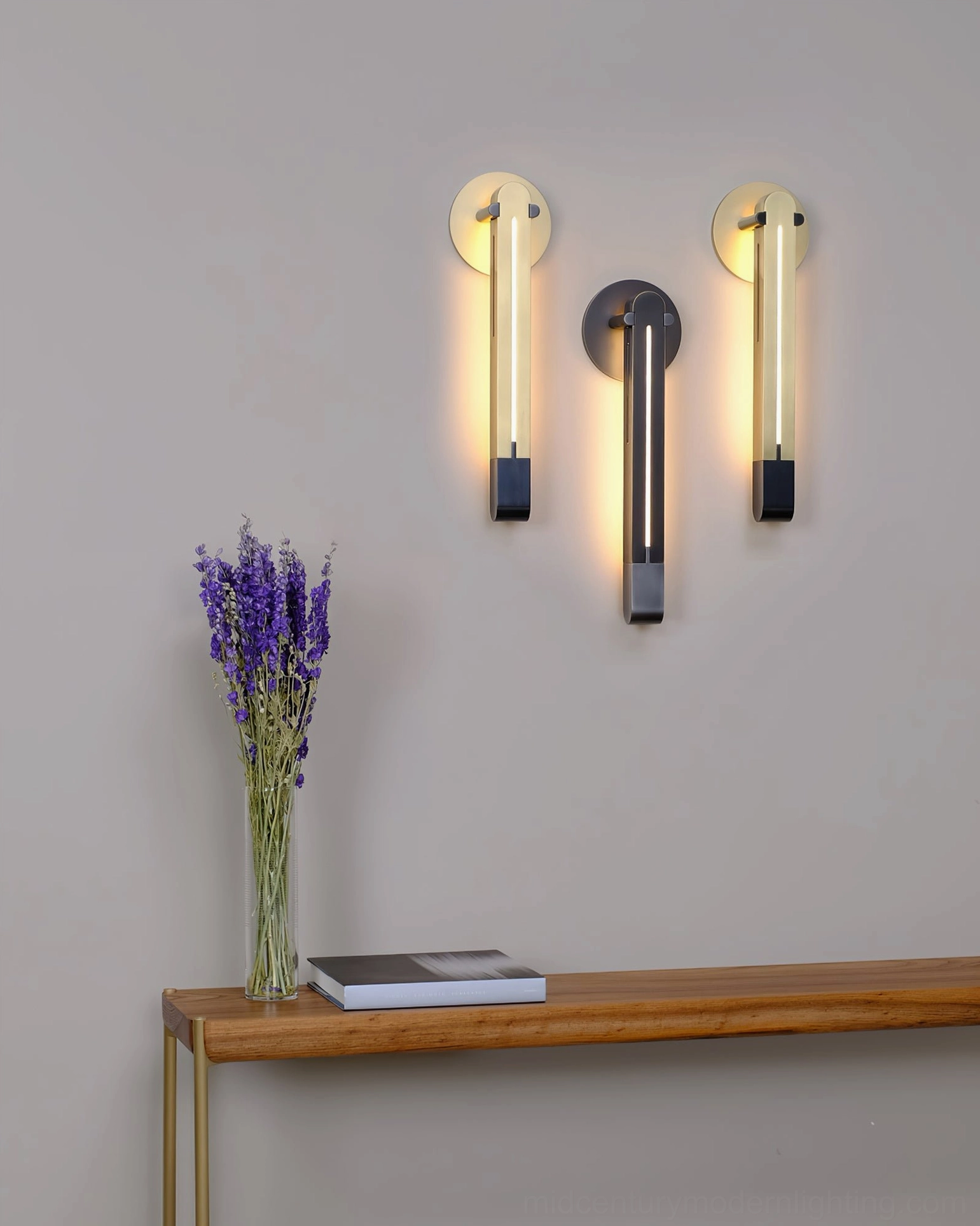 Three Torpedo sconces in black and brass mixed finishes installed in entryway with wooden console table and decorative lavender styling