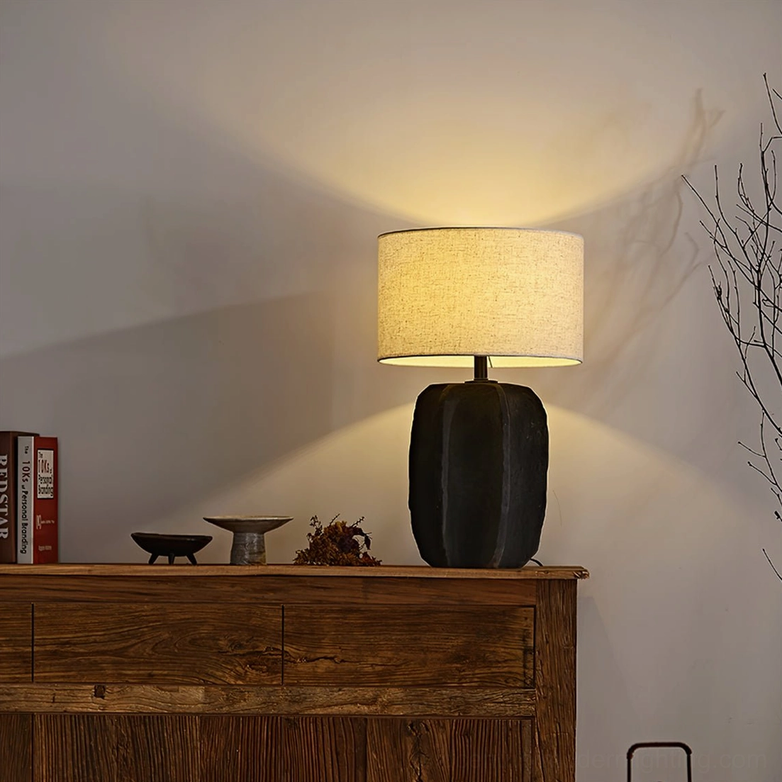 Torso table lamp side view with beige linen shade on wooden sideboard with books