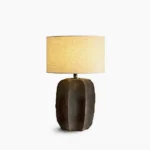 Torso ceramic table lamp with sculptural white base and beige fabric shade on pure white background