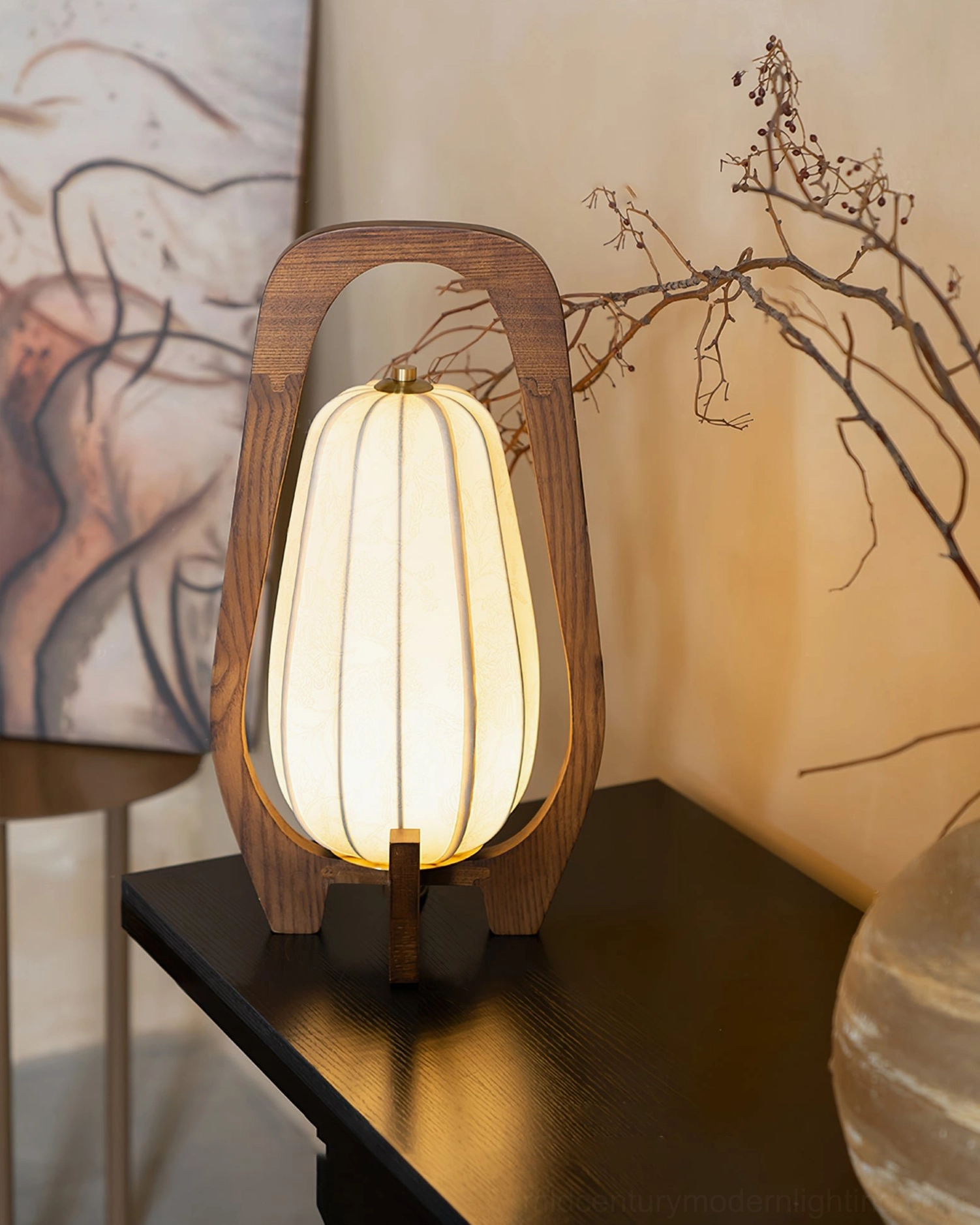 Totem table lamp styled on dark wood surface with artwork and botanical branches, three-quarter front angle