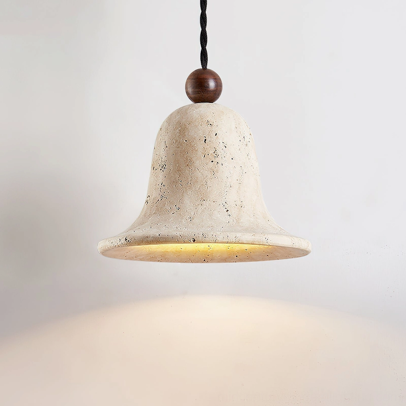 Low-angle view of illuminated travertine bell pendant with twisted black cord and warm interior glow
