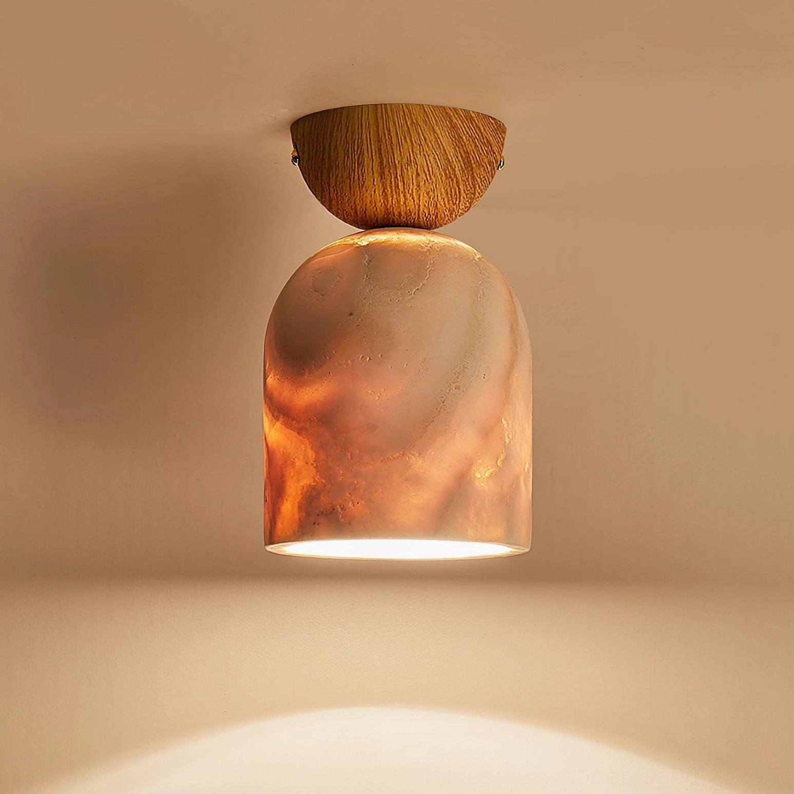 Lit travertine ceiling lamp with light wood mount and orange marbled glow on warm brown wall background