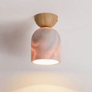 Illuminated travertine pendant lamp with light wood cap and pink marbled glowing shade against warm neutral wall