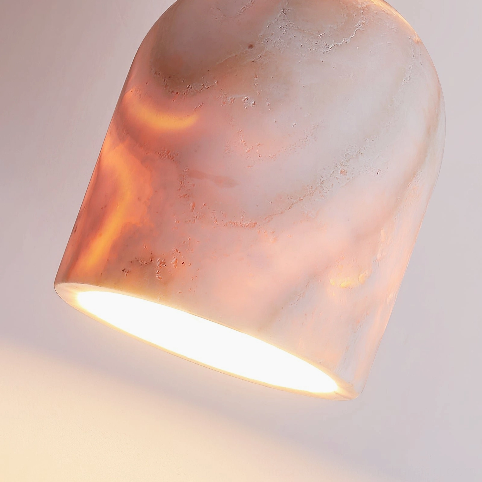 Close-up detail shot of pink marbled travertine lamp shade with warm interior glow showing porous stone texture
