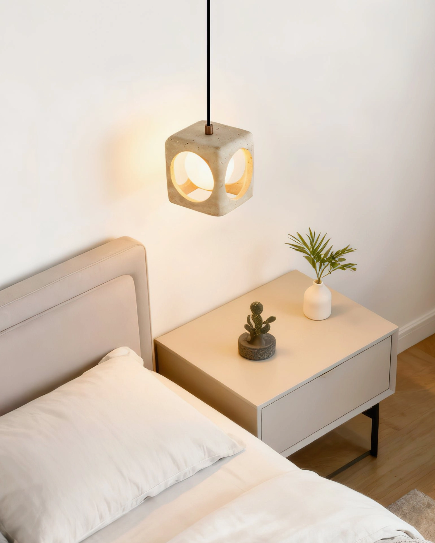 Low-angle side view of travertine pendant lamp hanging above bedside table with contemporary furnishings