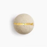 Round travertine wall sconce with natural crack detail, illuminated golden light, studio overhead view on white background
