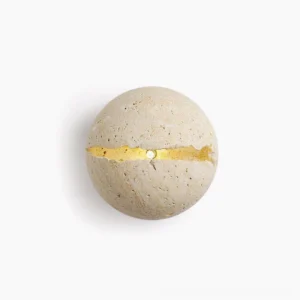 Round travertine wall sconce with natural crack detail, illuminated golden light, studio overhead view on white background