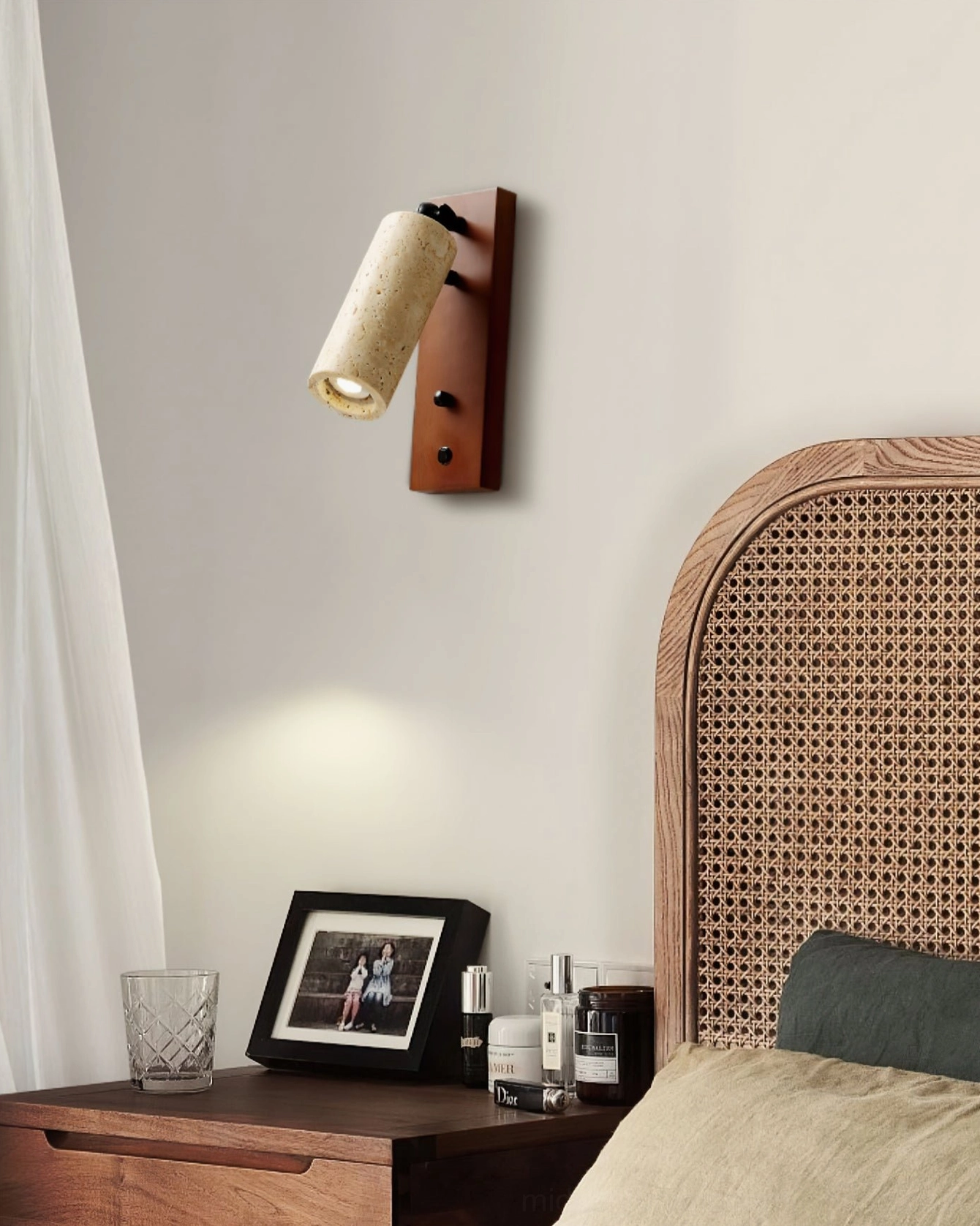 Travertine wall sconce installed in bedroom with rattan headboard and minimalist bedside styling