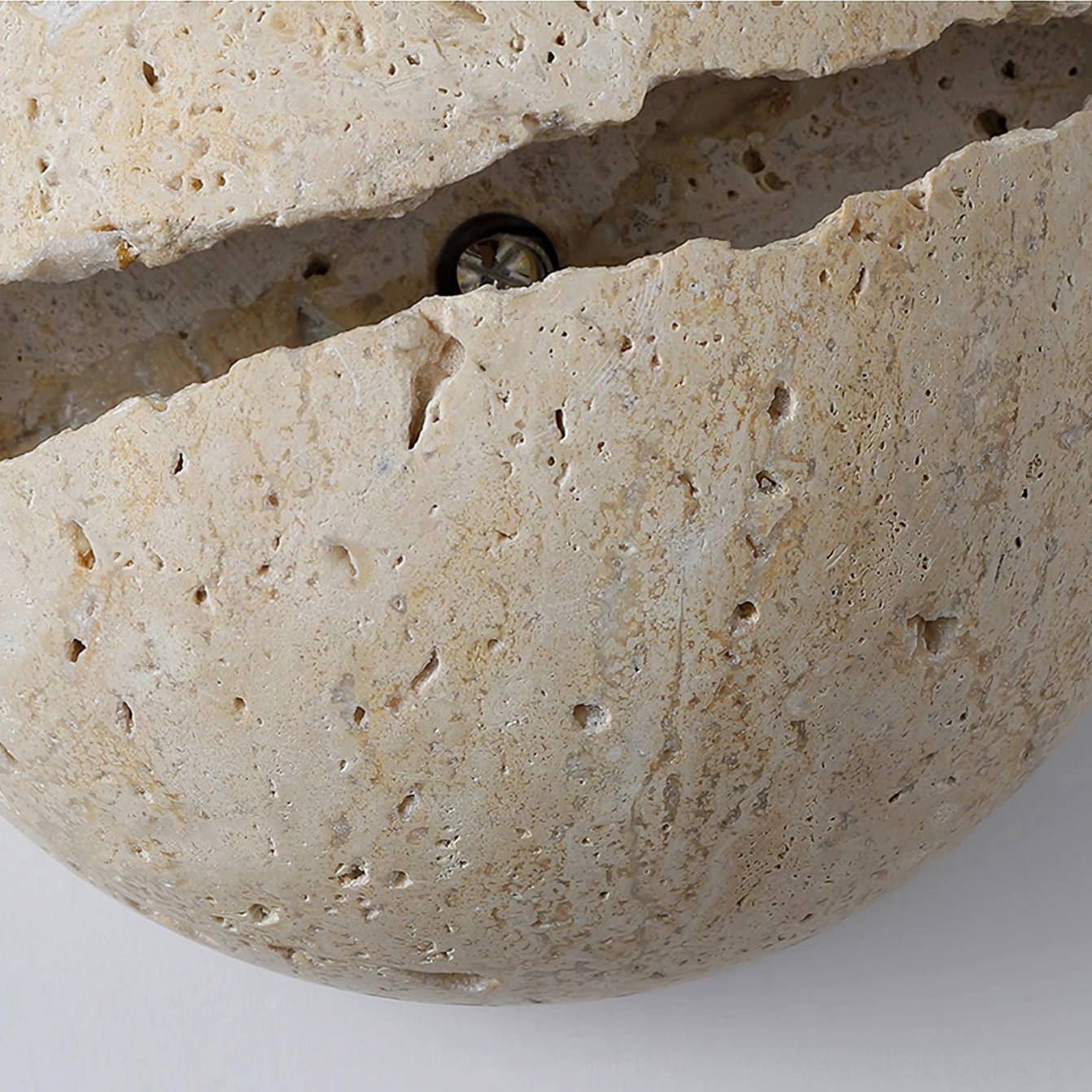 Macro side view of round travertine sconce showing rough stone surface and metal mounting hardware