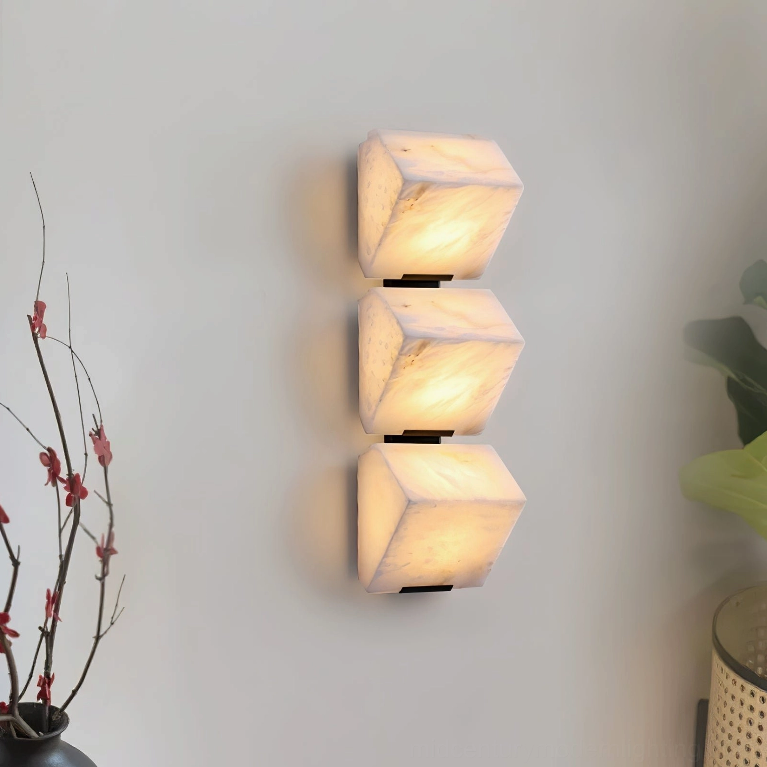 Three-light sculptural alabaster wall sconce in living room with floral plant, creating rhythmic vertical light composition