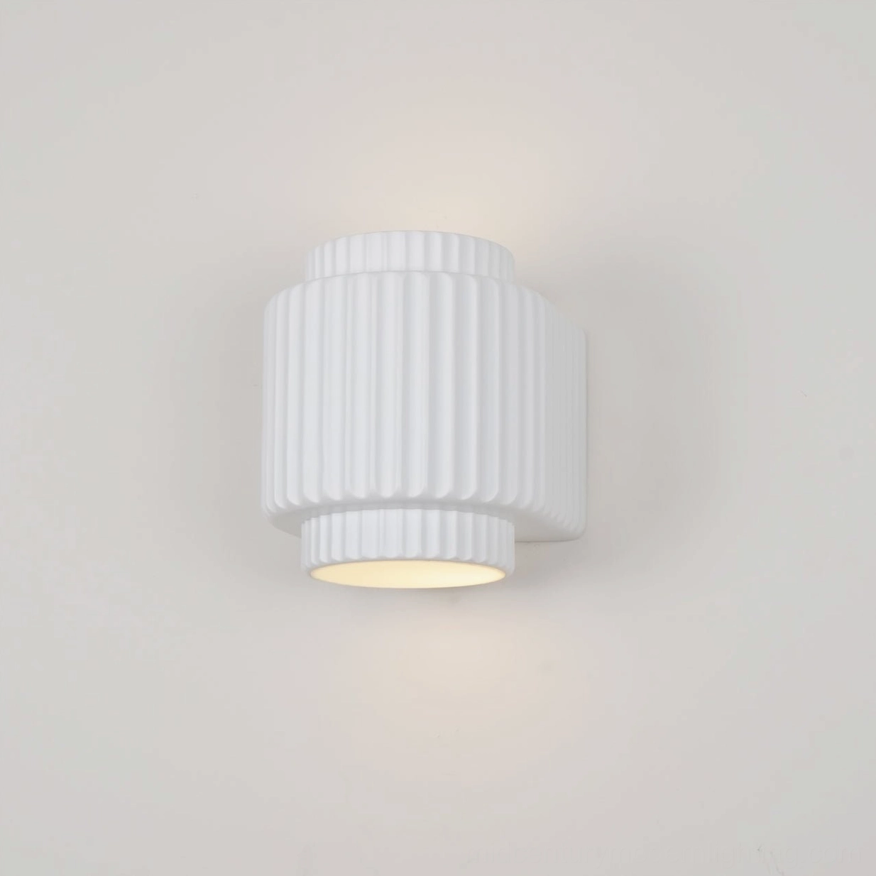 Tristan architectural wall lamp three-quarter view emitting warm light from bottom aperture with compact cylindrical form