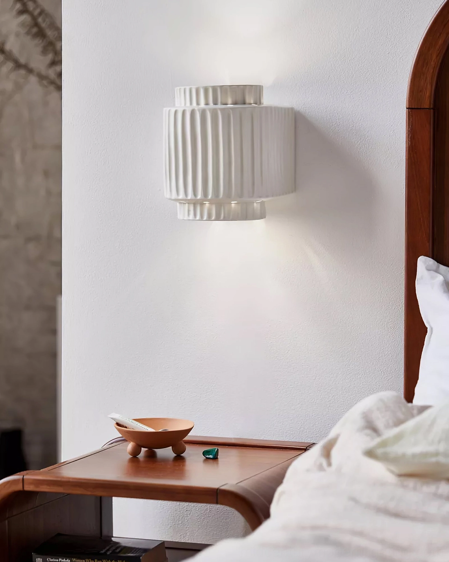 Tristan fluted wall sconce installed in minimalist Nordic bedroom with wooden bedside table and arched headboard