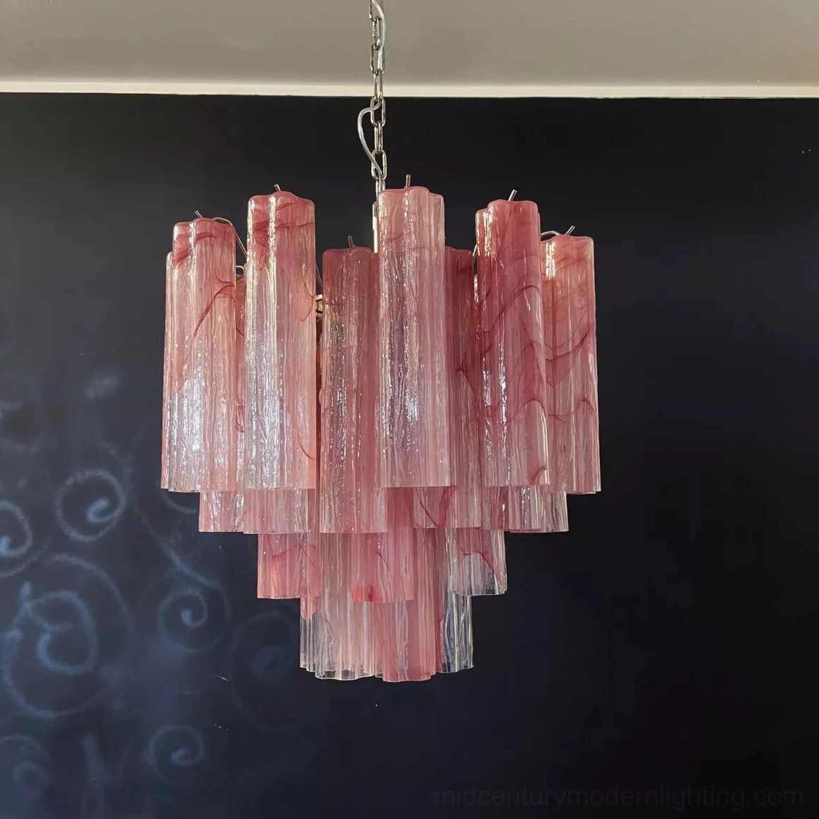 Pink tiered Murano-style chandelier with silver suspension chain against dark chalkboard wall background