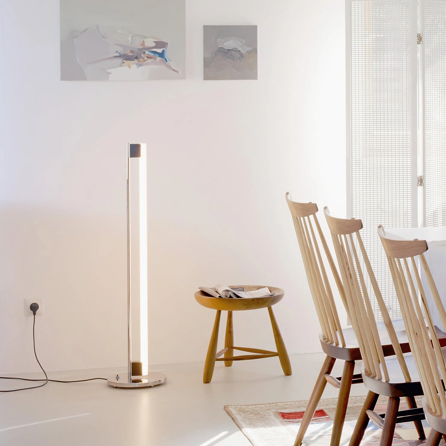Tube LED floor lamp creating warm ambient lighting in modern dining room with wooden chairs and neutral interior